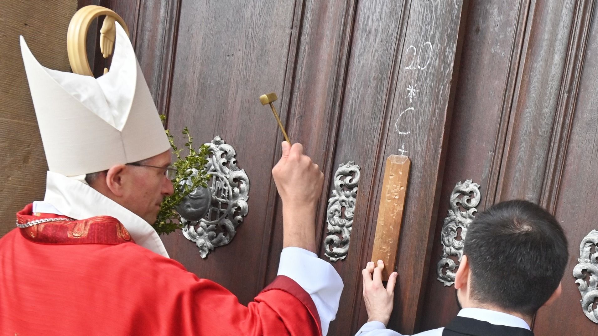 Mit einem kleinen Hämmerchen klopft Bischof Dr. Michael Gerber am Palmsonntag vor dem Einzug in den Dom symbolisch an das Domportal. Foto: Bistum Fulda / Dr. Arnulf Müller   